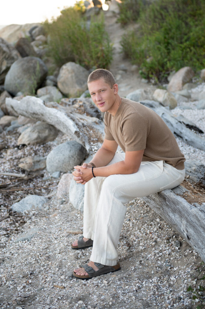 Senior photo sitting along driftwood on  the shoreline at Meigs Point, Hammonasset Beach State Park, Madison CT