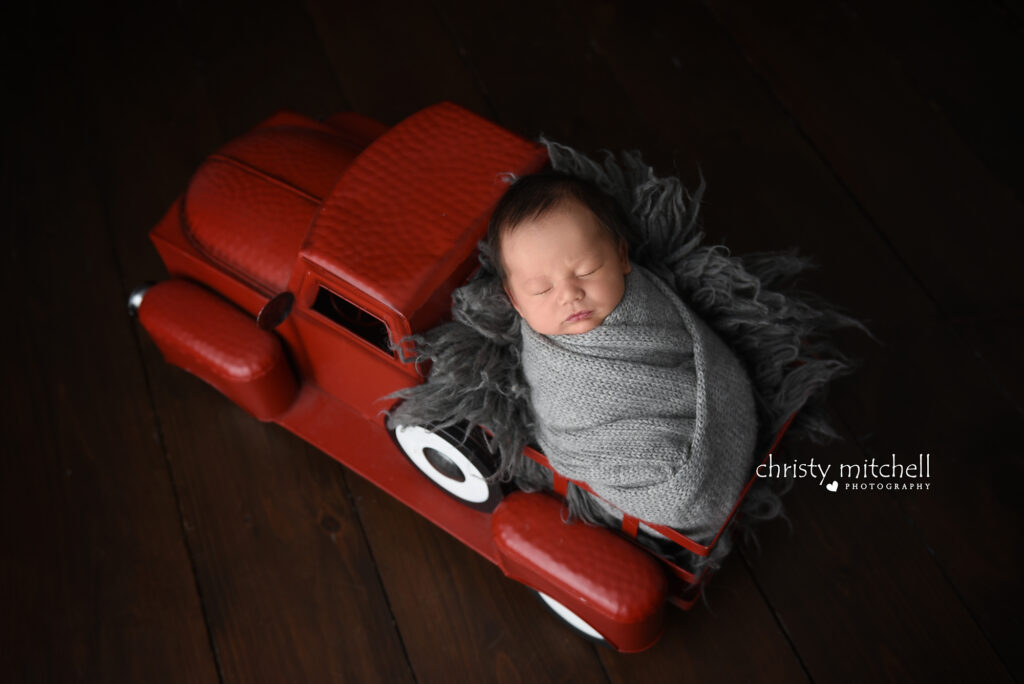 Baby Noah posed in red truck prop during newborn photography session in Wallingford Connecticut